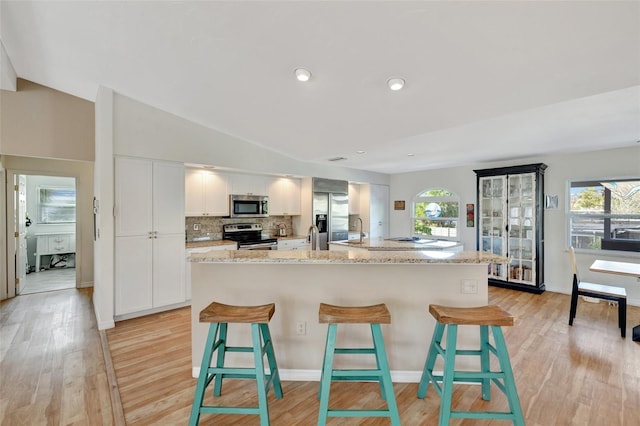 kitchen featuring a kitchen bar, a kitchen island with sink, white cabinets, and stainless steel appliances