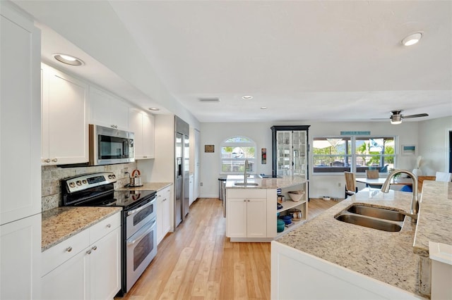 kitchen with light stone countertops, sink, stainless steel appliances, an island with sink, and white cabinets