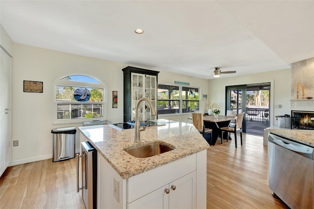 kitchen featuring dishwasher, a center island with sink, white cabinets, ceiling fan, and light stone counters