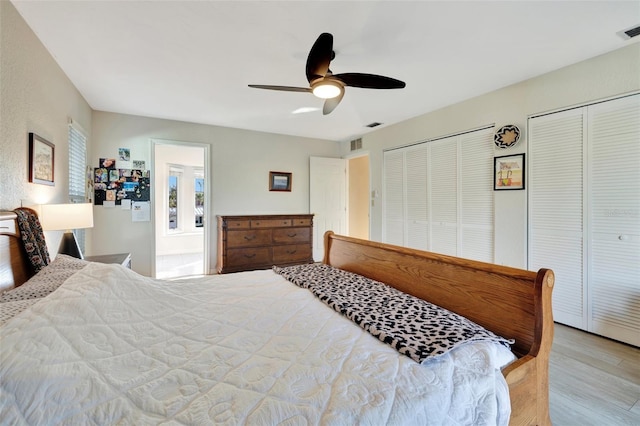 bedroom with ceiling fan, light hardwood / wood-style flooring, and multiple closets