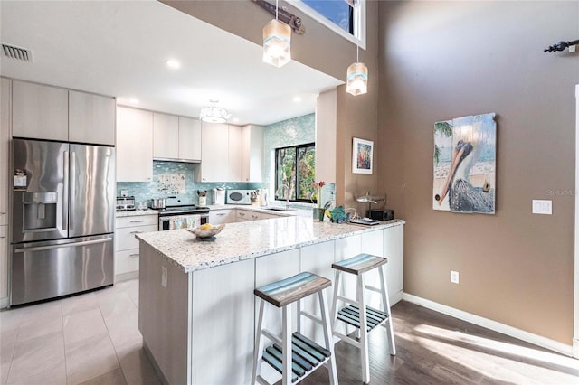 kitchen with light stone countertops, white cabinets, appliances with stainless steel finishes, decorative light fixtures, and kitchen peninsula