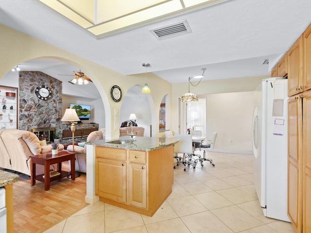 kitchen with light tile patterned floors, white fridge, light stone counters, and ceiling fan