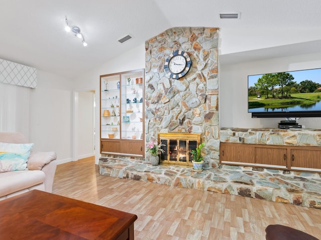 living room featuring a stone fireplace, light hardwood / wood-style flooring, and vaulted ceiling