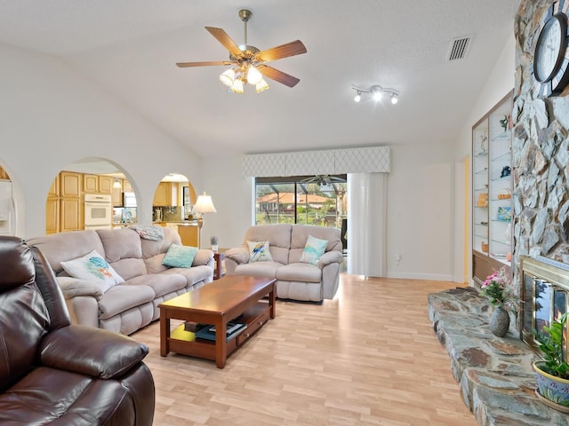 living room featuring ceiling fan, a stone fireplace, light hardwood / wood-style flooring, and vaulted ceiling