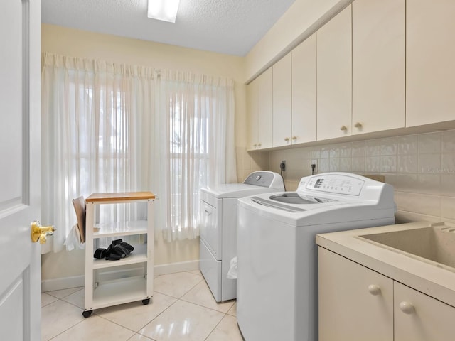 laundry room with cabinets, a textured ceiling, washer and clothes dryer, and light tile patterned flooring