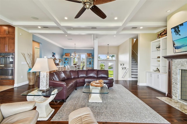 living room featuring ceiling fan with notable chandelier, beam ceiling, dark wood-type flooring, and coffered ceiling