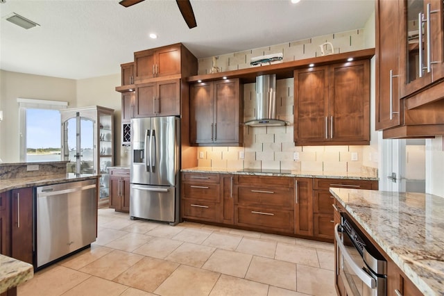 kitchen with light stone countertops, appliances with stainless steel finishes, decorative backsplash, wall chimney exhaust hood, and ceiling fan