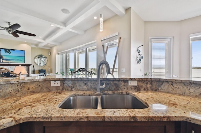 kitchen featuring ceiling fan, sink, coffered ceiling, light stone counters, and beamed ceiling