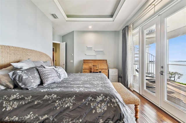 bedroom featuring a tray ceiling, access to exterior, hardwood / wood-style floors, and french doors