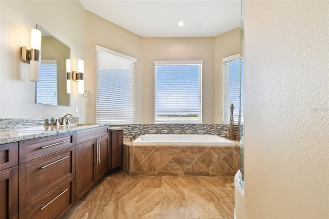 bathroom featuring vanity, a wealth of natural light, and a relaxing tiled tub