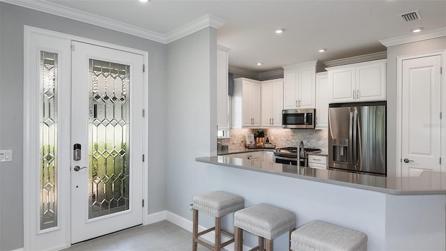 kitchen with white cabinetry, stainless steel appliances, kitchen peninsula, light tile patterned flooring, and ornamental molding