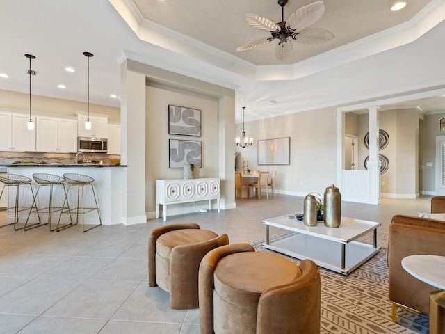 living room with a tray ceiling, crown molding, light tile patterned floors, and ceiling fan with notable chandelier