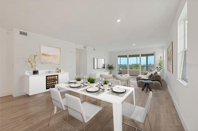 dining space with bar area, beverage cooler, and light wood-type flooring