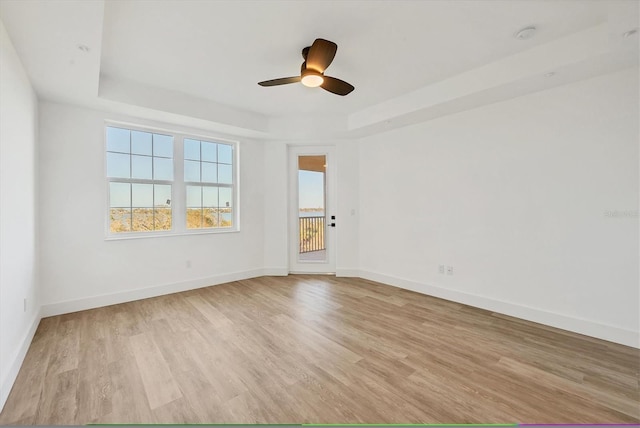 spare room with light wood-type flooring, a tray ceiling, and ceiling fan