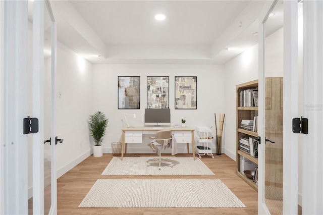 home office featuring a raised ceiling, light wood-type flooring, and french doors