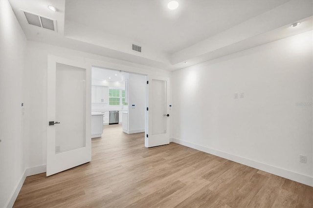 spare room featuring a raised ceiling, light wood-type flooring, and french doors