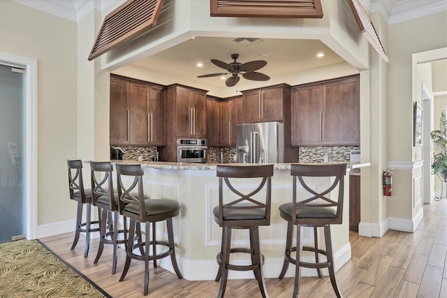 kitchen featuring crown molding, a breakfast bar area, decorative backsplash, light hardwood / wood-style floors, and stainless steel appliances