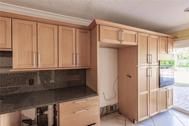 kitchen with tasteful backsplash, crown molding, dark stone countertops, oven, and light tile patterned flooring