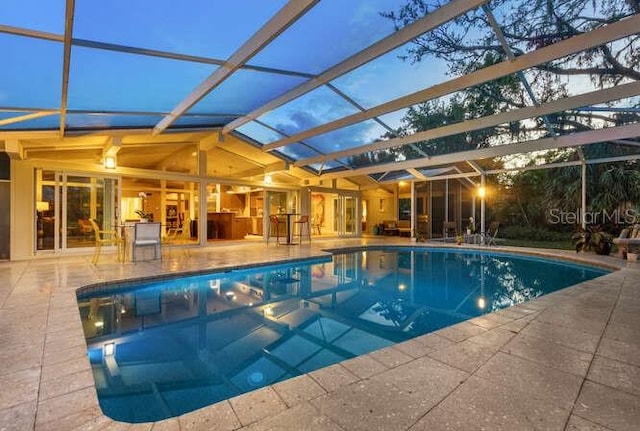 pool at dusk featuring a patio area and glass enclosure