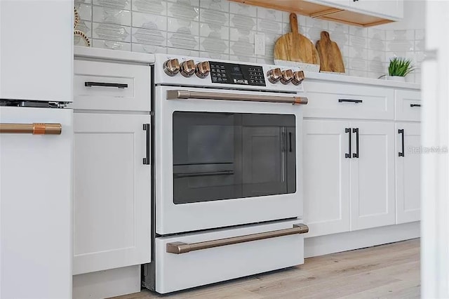 room details with white cabinets, white range with electric cooktop, tasteful backsplash, and light hardwood / wood-style flooring