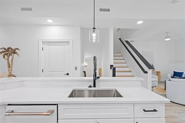 kitchen featuring light wood-type flooring, ceiling fan, sink, pendant lighting, and white cabinets