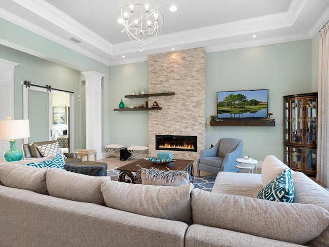 living room with a fireplace, a barn door, a raised ceiling, and crown molding