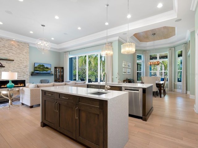 kitchen with a raised ceiling, pendant lighting, stainless steel dishwasher, and a center island with sink