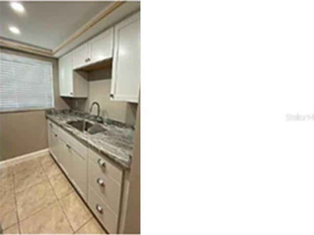 kitchen with white cabinets, light tile patterned flooring, light stone counters, and sink