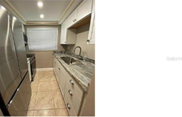 kitchen featuring sink, light tile patterned floors, light stone countertops, range, and stainless steel refrigerator