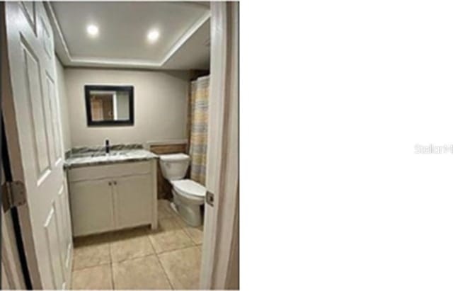 bathroom featuring a raised ceiling, tile patterned flooring, vanity, and toilet