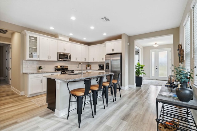 kitchen featuring white cabinetry, stainless steel appliances, light stone counters, a breakfast bar area, and a center island with sink