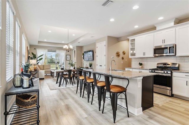 kitchen with appliances with stainless steel finishes, a raised ceiling, an inviting chandelier, a breakfast bar area, and an island with sink