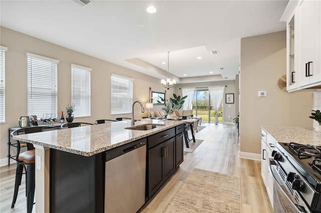 kitchen featuring a center island with sink, sink, a tray ceiling, white cabinetry, and stainless steel appliances