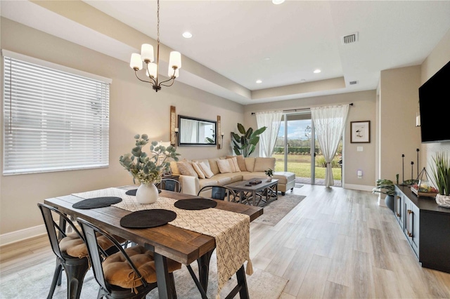 dining space featuring a tray ceiling, an inviting chandelier, and light hardwood / wood-style flooring