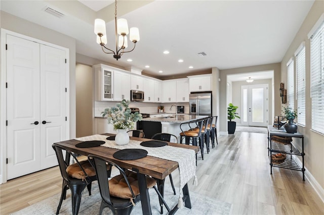 dining space with sink, light hardwood / wood-style flooring, and an inviting chandelier