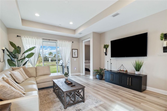 living room with a raised ceiling and light hardwood / wood-style flooring