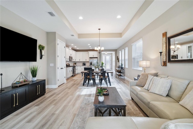 living room featuring a tray ceiling, light hardwood / wood-style flooring, and a notable chandelier