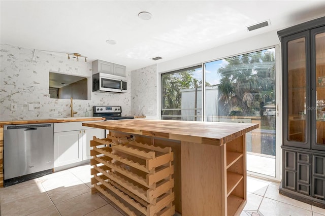 kitchen with light tile patterned floors, white cabinets, appliances with stainless steel finishes, and wooden counters