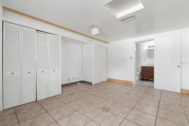 unfurnished bedroom with multiple closets, light tile patterned flooring, and ensuite bath