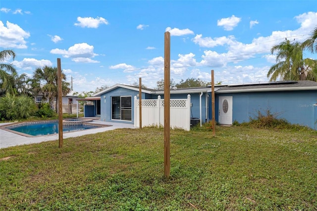 back of house with a yard, a swimming pool with hot tub, and solar panels