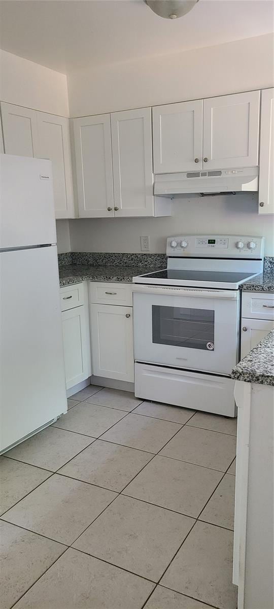 kitchen with white cabinets, white appliances, dark stone countertops, and light tile patterned flooring