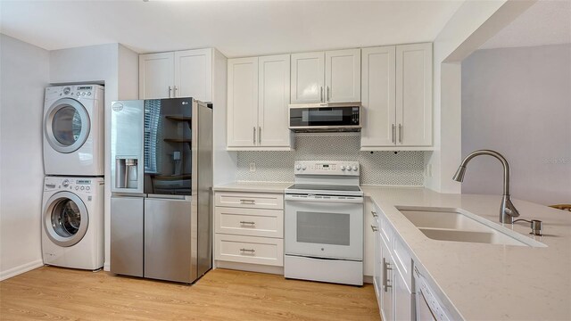 kitchen featuring stacked washing maching and dryer, stainless steel appliances, white cabinets, and sink