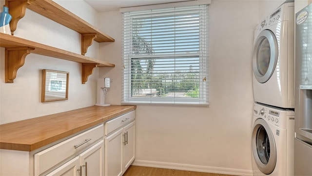 clothes washing area with stacked washer / drying machine, cabinets, plenty of natural light, and light hardwood / wood-style flooring