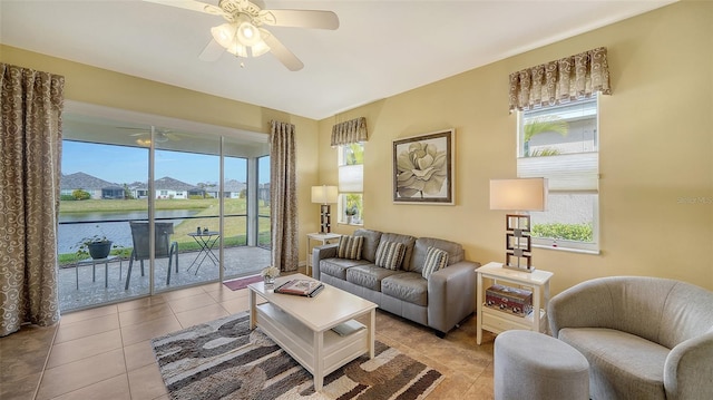 tiled living room featuring ceiling fan, a water view, and a healthy amount of sunlight