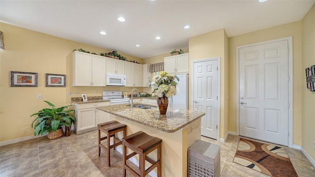 kitchen featuring light stone counters, a breakfast bar, white appliances, a kitchen island with sink, and sink