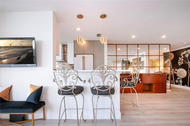 kitchen with kitchen peninsula, light wood-type flooring, high end white fridge, pendant lighting, and a breakfast bar area