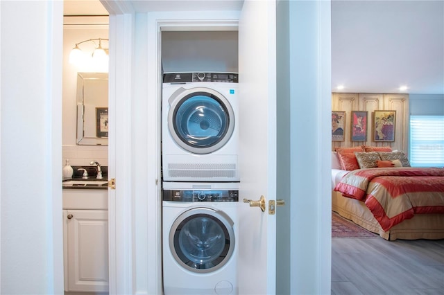 clothes washing area featuring sink, wood-type flooring, and stacked washer and clothes dryer