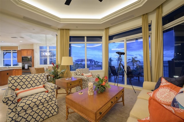 living room with ceiling fan with notable chandelier, ornamental molding, sink, and a tray ceiling