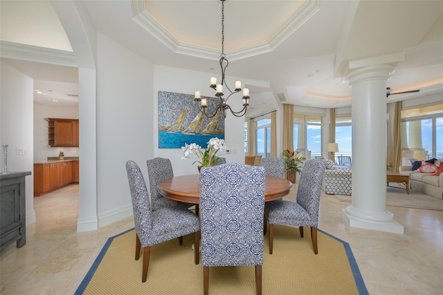 dining room with a raised ceiling, an inviting chandelier, and ornate columns