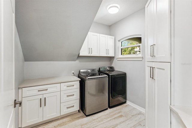 clothes washing area featuring washing machine and clothes dryer, light hardwood / wood-style flooring, cabinets, and a textured ceiling